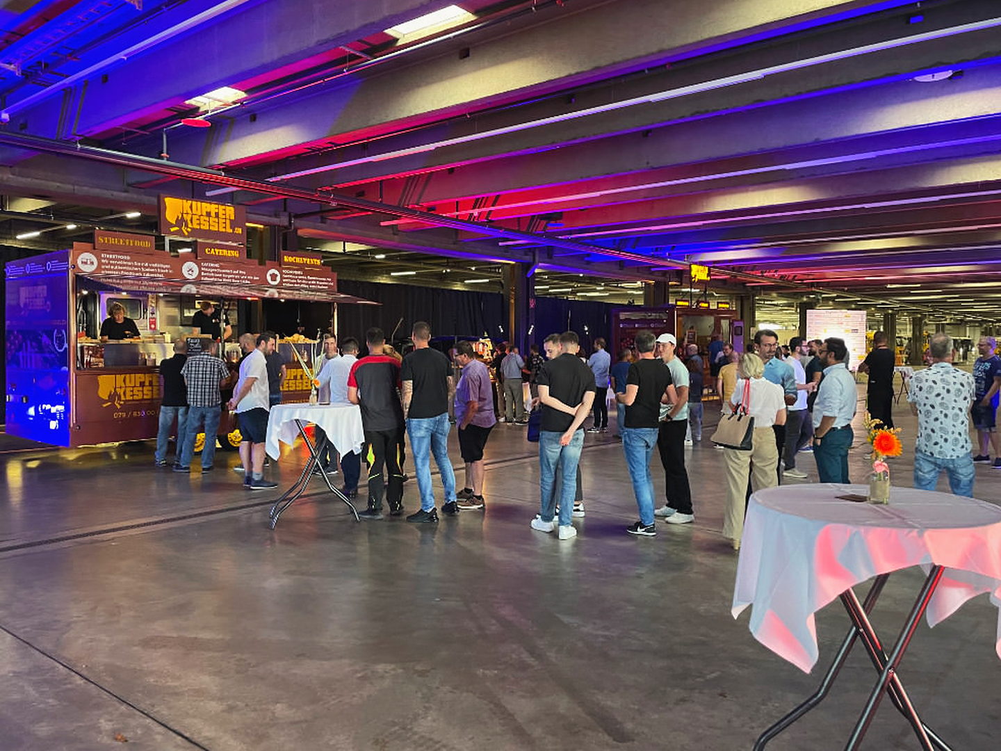 Gäste vor dem Kupferkessel-Foodtruck in einer farbig beleuchteten Halle