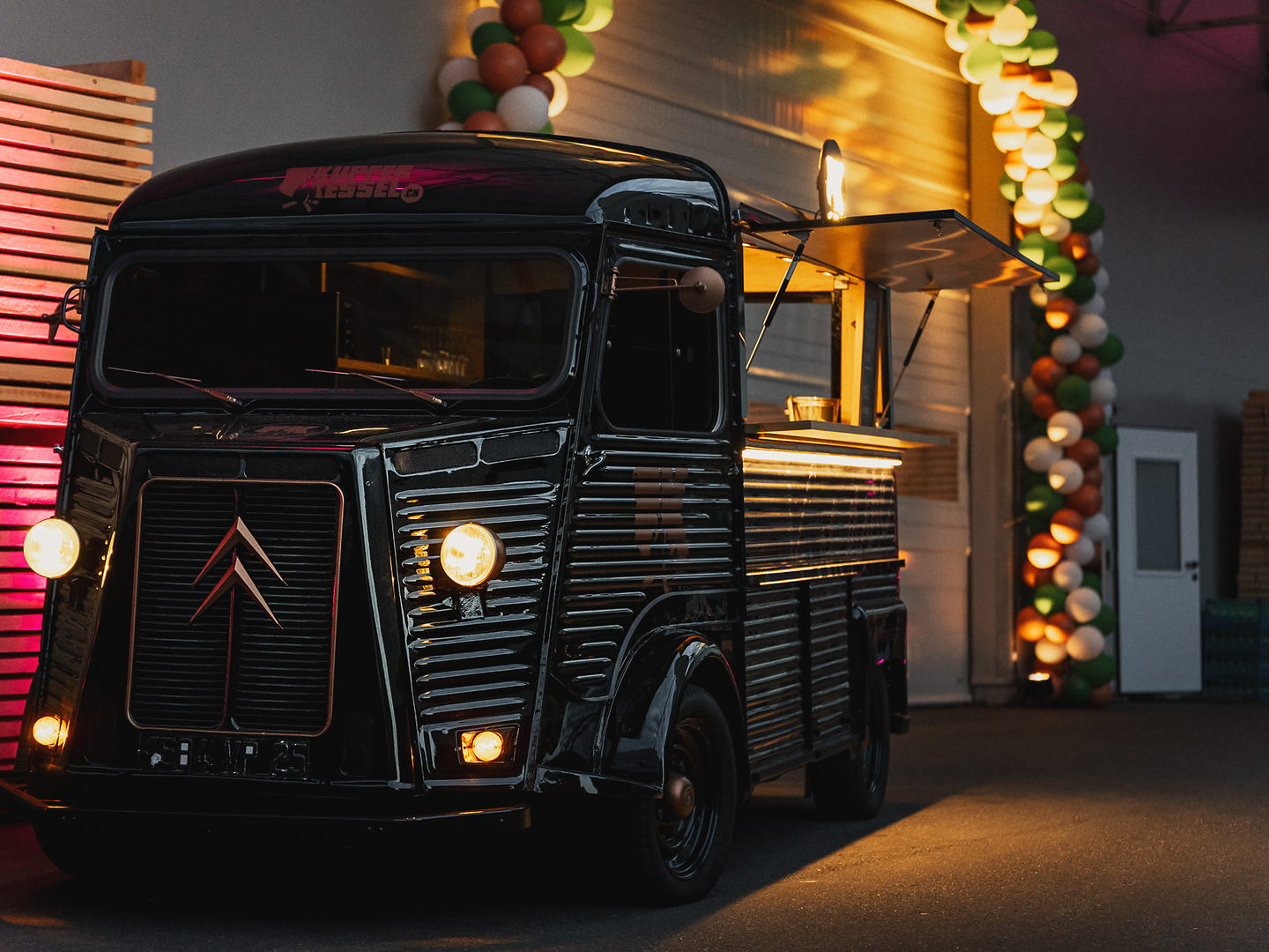 Schwarzer Kupferkessel-Foodtruck mit offener Theke vor einer Ballongirlande