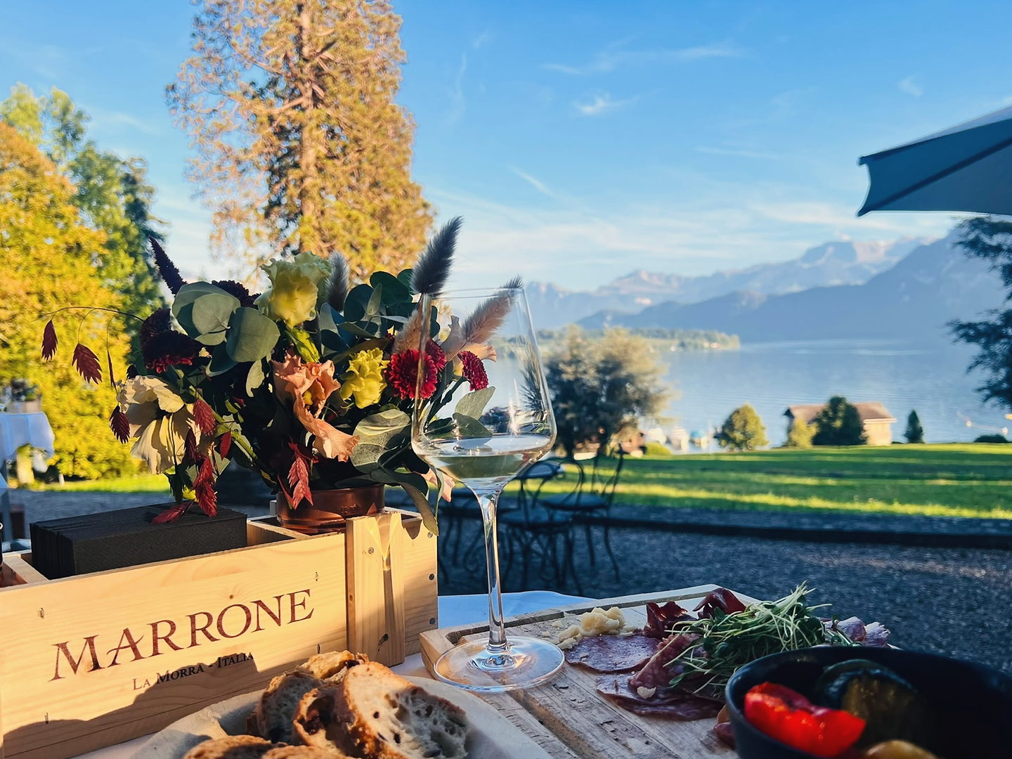 Apéro mit Weinglas, Blumen und Antipasti vor Seepanorama