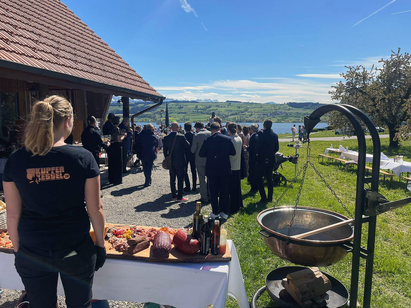 Apéro im Freien am See mit Kupferkessel-Team, Antipasti-Brett, Kupferkessel über dem Feuer und Gästen