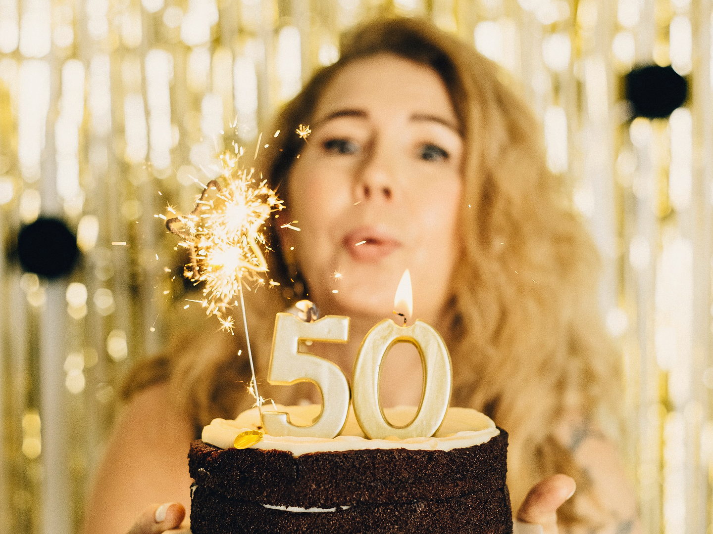 Frau bläst die Kerze einer Torte mit der Zahl 50 aus, daneben eine Wunderkerze