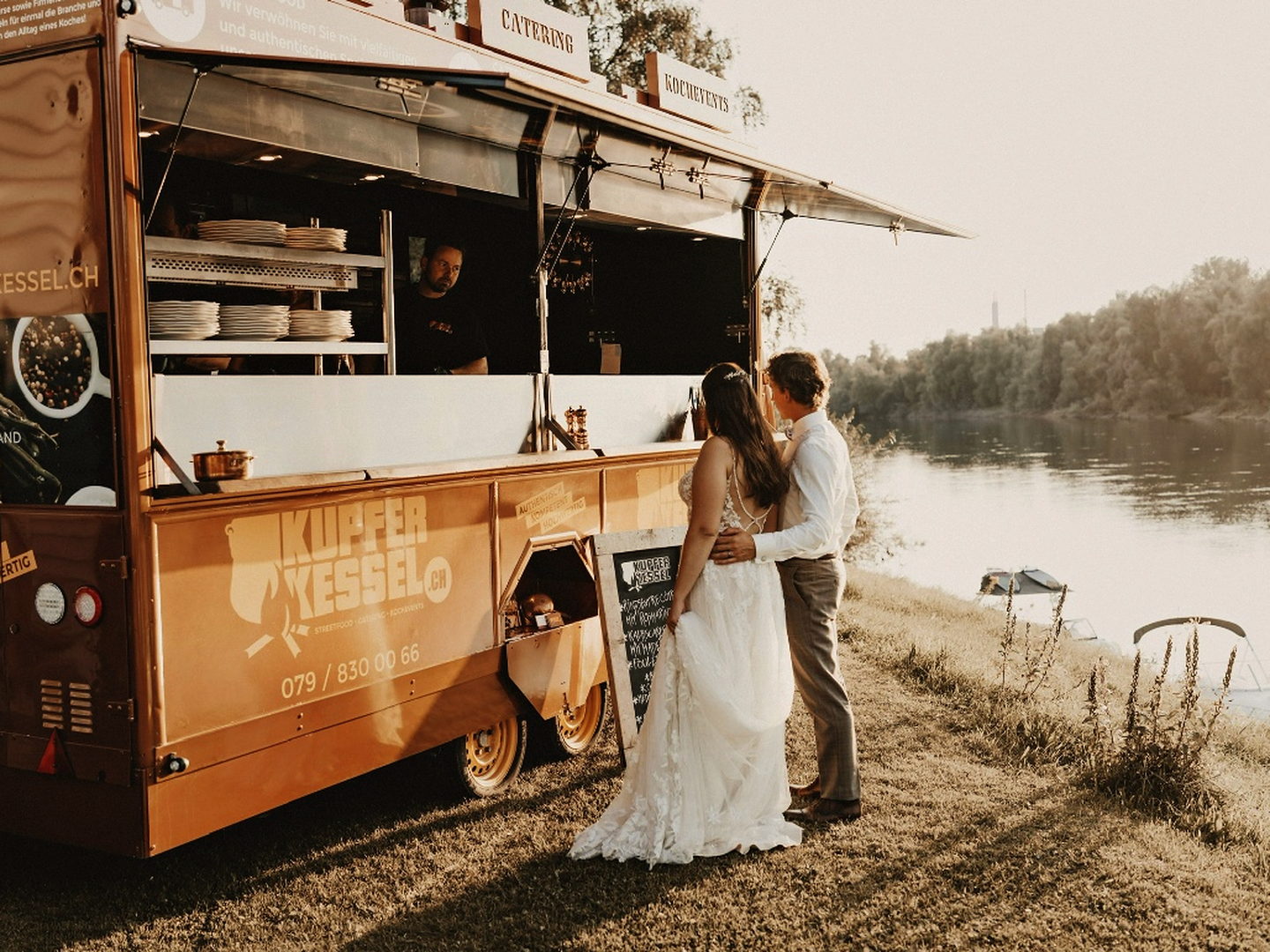 Brautpaar vor dem Kupferkessel-Foodtruck am Seeufer im Abendlicht